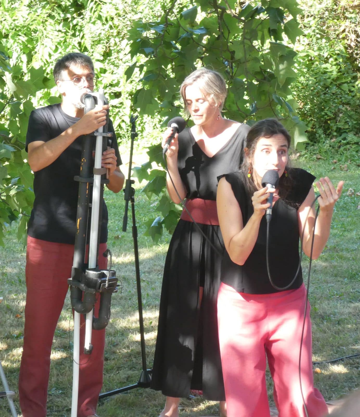 Le Trio Volubile en plein chant : un musicien souffle dans un instrument fait de tuyaux, les deux chanteuses à ses côtés